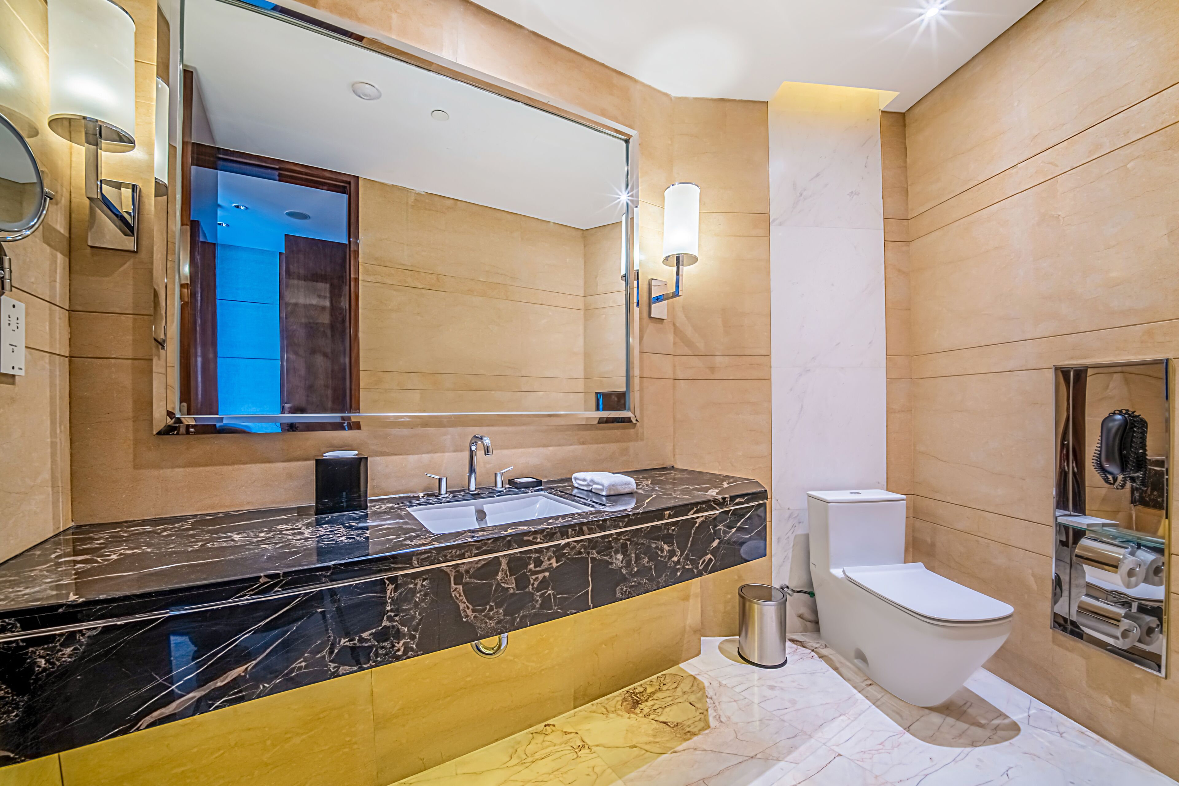 A modern bathroom with a black marble sink, a mirror, a toilet, and a towel rack.