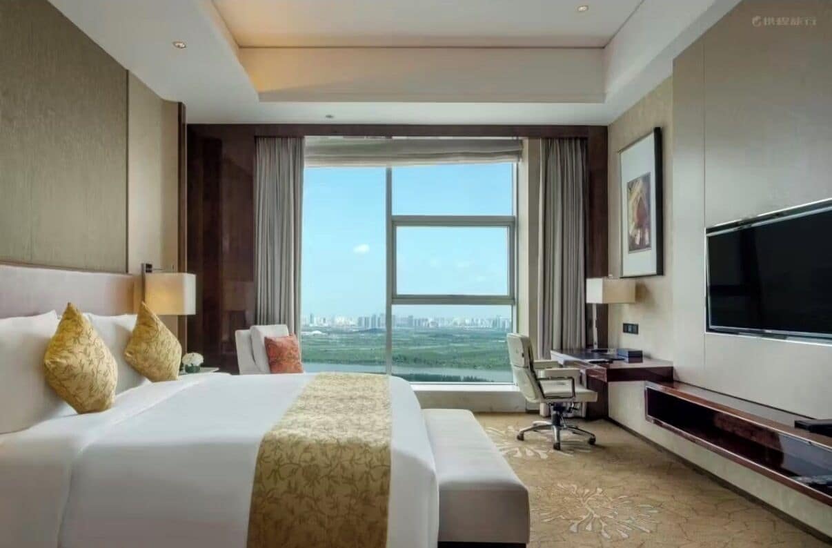 Habitación de hotel con una cama grande, un escritorio, una silla, un televisor y vista a la ciudad.