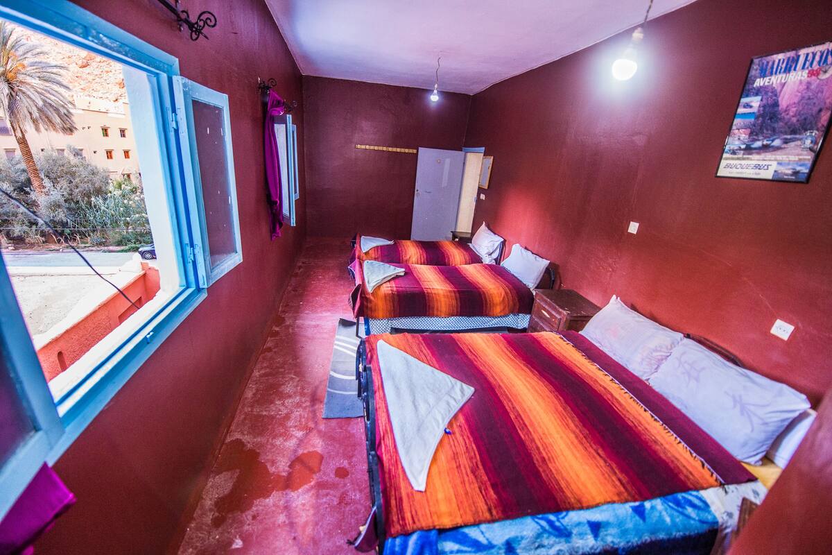 Une chambre avec deux lits, une fenêtre, une porte et une affiche au mur.