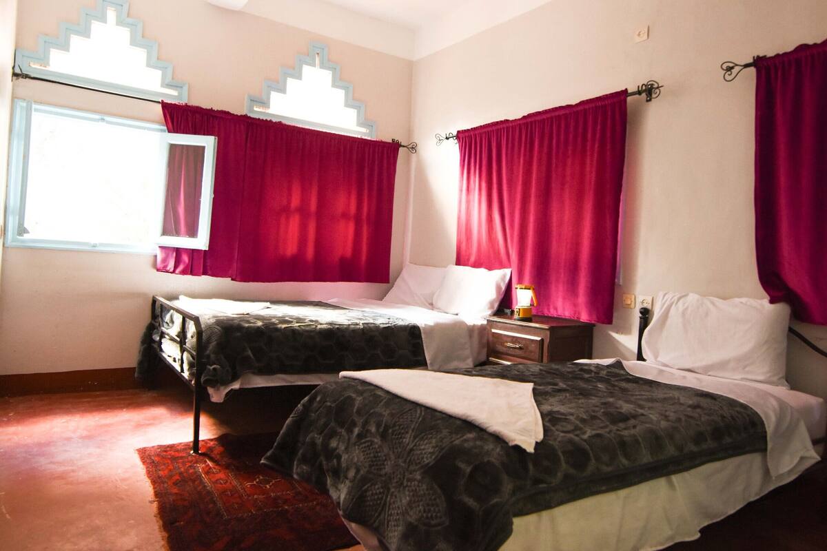 Une chambre avec deux lits, une fenêtre avec un miroir et des rideaux rouges.