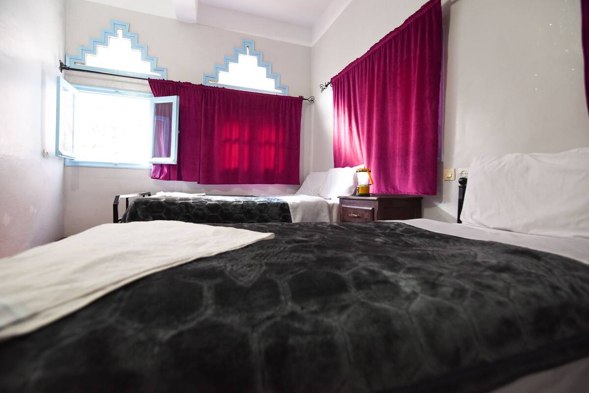 Une chambre à coucher avec un lit, une table de chevet, une lampe et une fenêtre avec des rideaux.