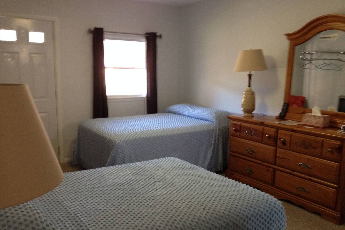 A bedroom with two beds, a dresser, a lamp, and a window with curtains.