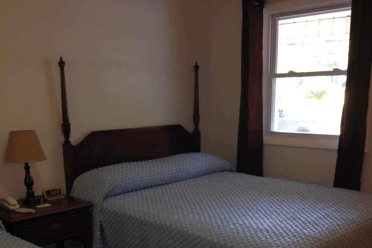 A bedroom with two single beds, a nightstand with a lamp, a clock, and a window with curtains.