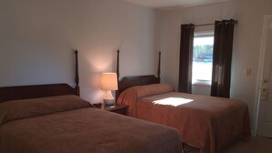 A hotel room with two beds, a nightstand with a lamp, and a window with curtains. - McGregor Inn Motel (Gansevoort)