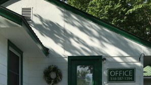 A white building with a green door, a sign reading "OFFICE 518-587-1394", and a small porch with white railings and steps. - McGregor Inn Motel (Gansevoort)