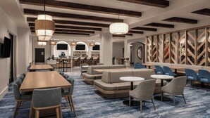 Een moderne hotellobby met een lange houten receptiebalie, comfortabele zithoeken en een bar op de achtergrond.