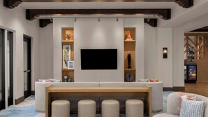 Een moderne woonkamer met een grote flatscreen televisie aan de muur, een houten bank en meerdere poefs.