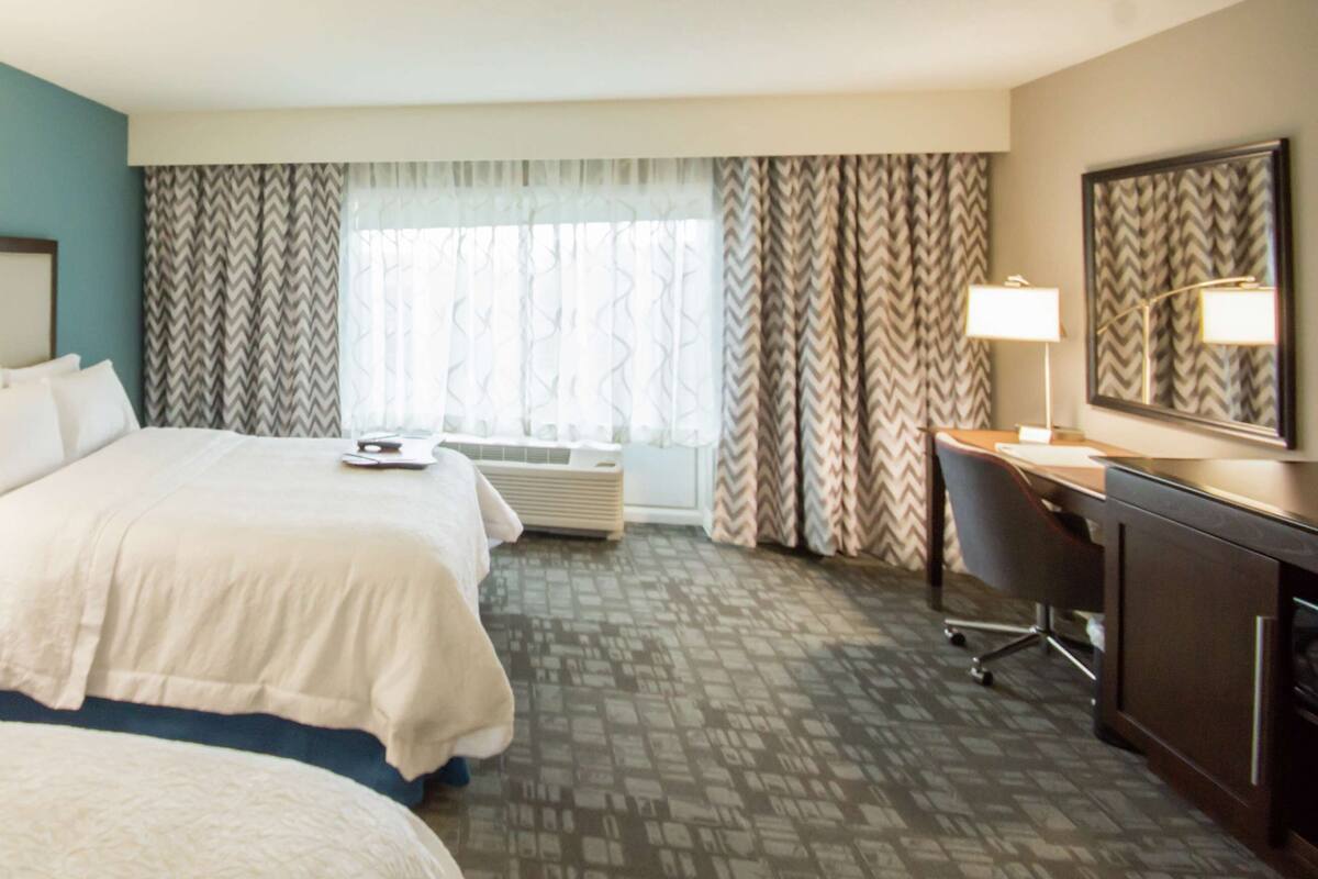A hotel room with two beds, a desk, a chair, a desk lamp, a telephone, and a large mirror.