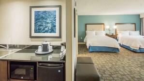 Ein Hotelzimmer mit Küchenzeile, zwei Betten, einem großen gerahmten Bild und einem gemusterten Teppich.