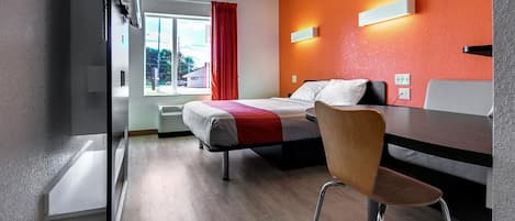 Una habitación de hotel con cama, una silla, un escritorio y un ventanal con cortinas.