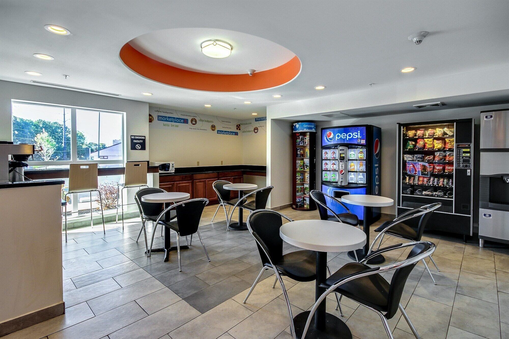 A modern cafe with round tables and black chairs, a Pepsi vending machine, and a no smoking sign.