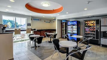 A modern cafe with round tables and black chairs, a Pepsi vending machine, and a no smoking sign.