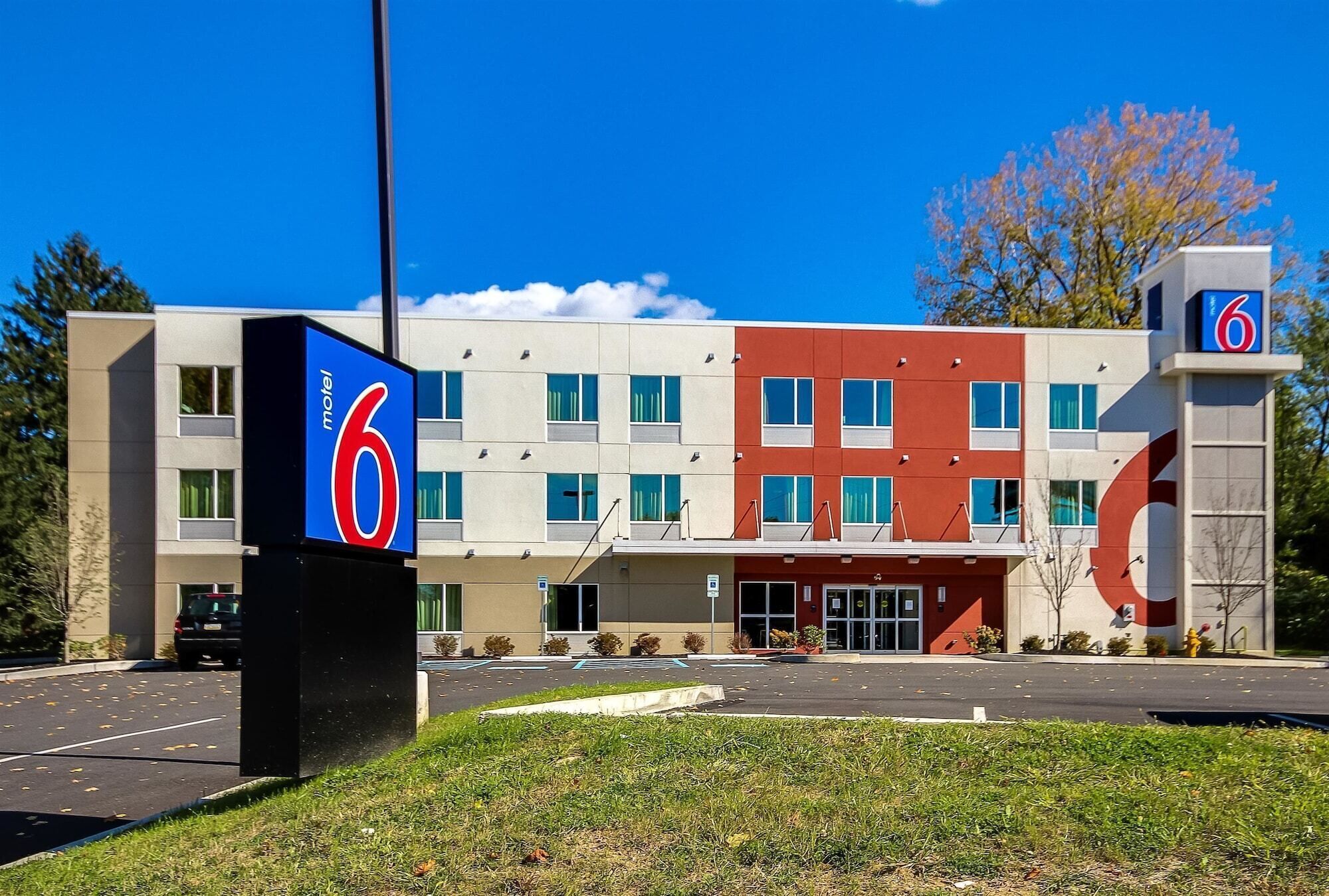 A motel with a modern design, featuring a prominent '6' sign, a parking lot, and a building with multiple windows.