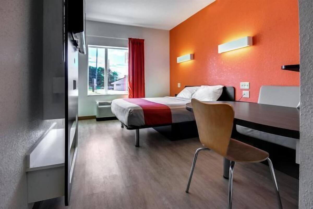 A hotel room with a bed, a desk, a chair, a window with a view, and a red curtain.