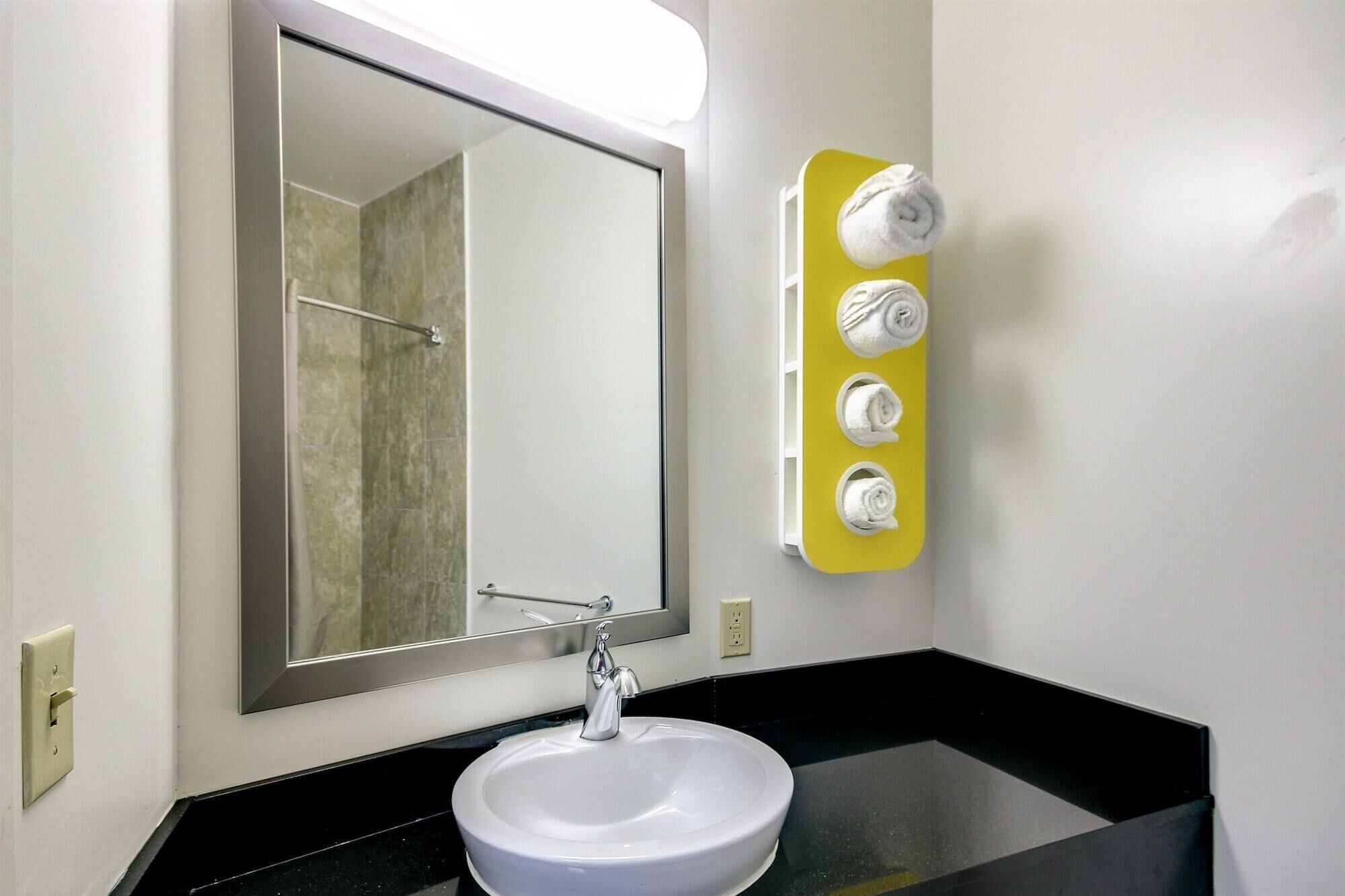 Un baño con un lavabo blanco, un espejo grande y un toallero amarillo con tres toallas.