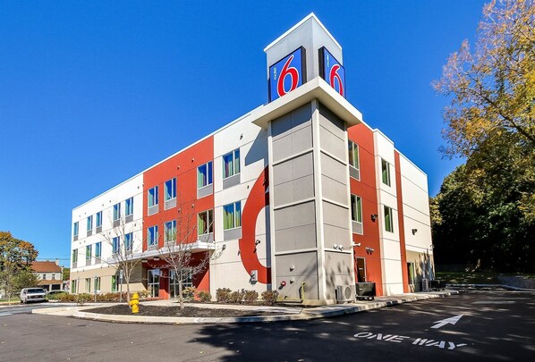 A modern hotel with a prominent '6' logo, a parking lot, and a 'ONE WAY' sign.