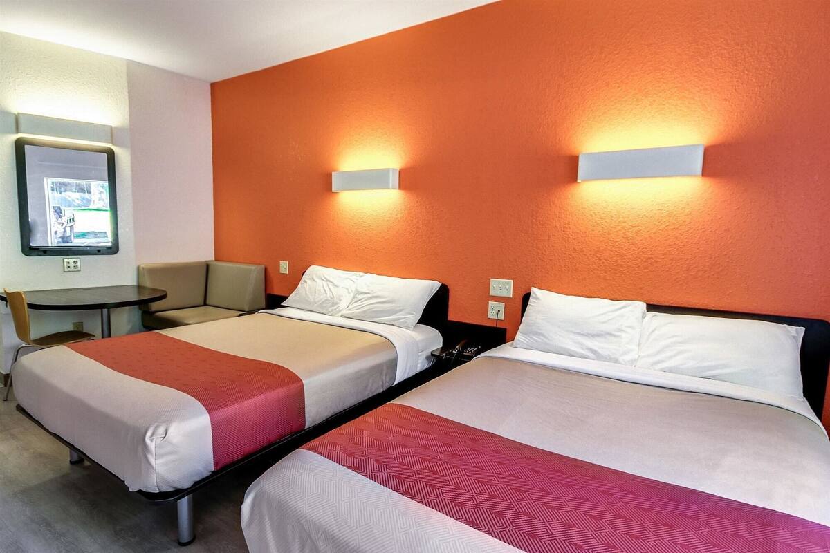 A hotel room with two beds, a small table, and a chair.