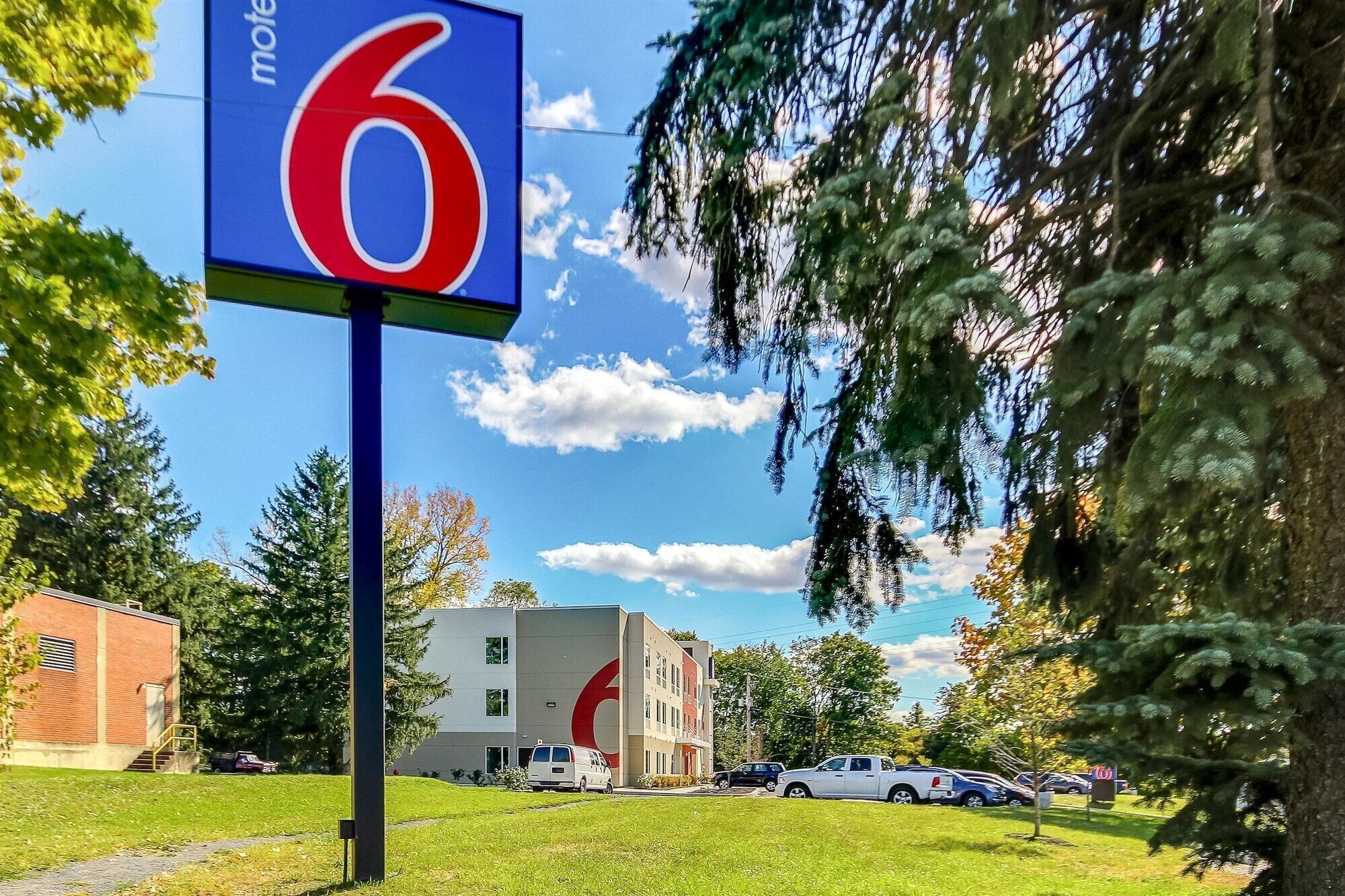 A motel sign with the number 6, a parking lot with several cars, and a building with a red and white logo in the background.