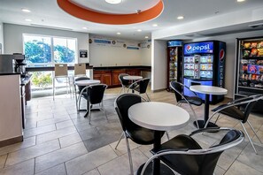 A restaurant with round tables and black chairs, a kitchen area, and a Pepsi vending machine.