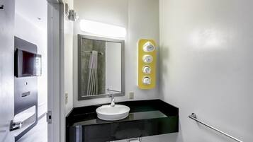 A modern bathroom with a black sink, a mirror, a towel dispenser, and a toilet.