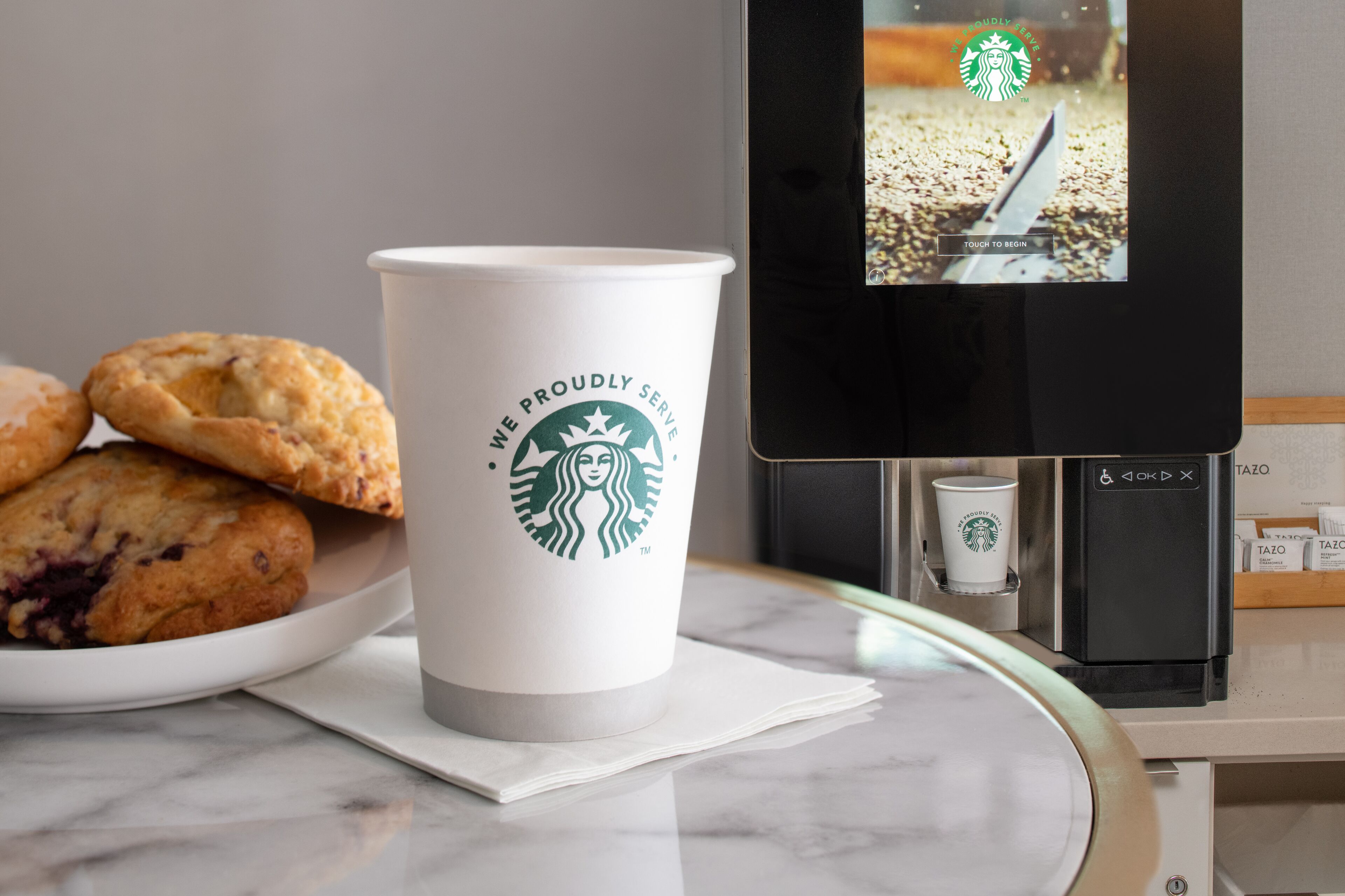 A Starbucks cup, a pastry, and a coffee machine on a marble countertop.