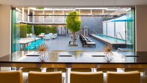 A modern indoor pool area with a glass partition, lounge chairs, and a central tree. - Hotel Lucent (Menlo Park)