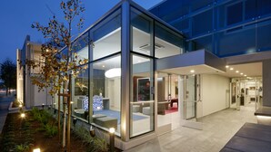 A modern building with glass walls, a seating area, and a well-lit entrance. - Hotel Lucent (Menlo Park)