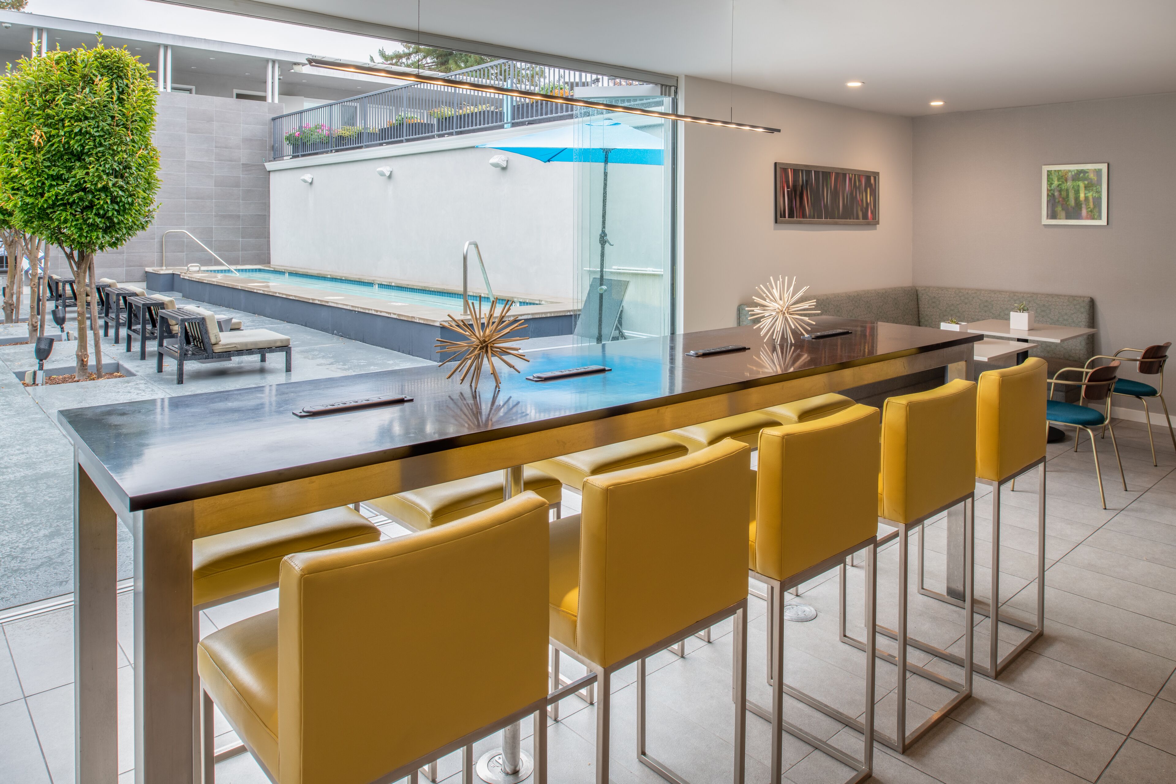 Zona de bar moderna con vista a la piscina, con taburetes y un área de estar con mesa y sillas.