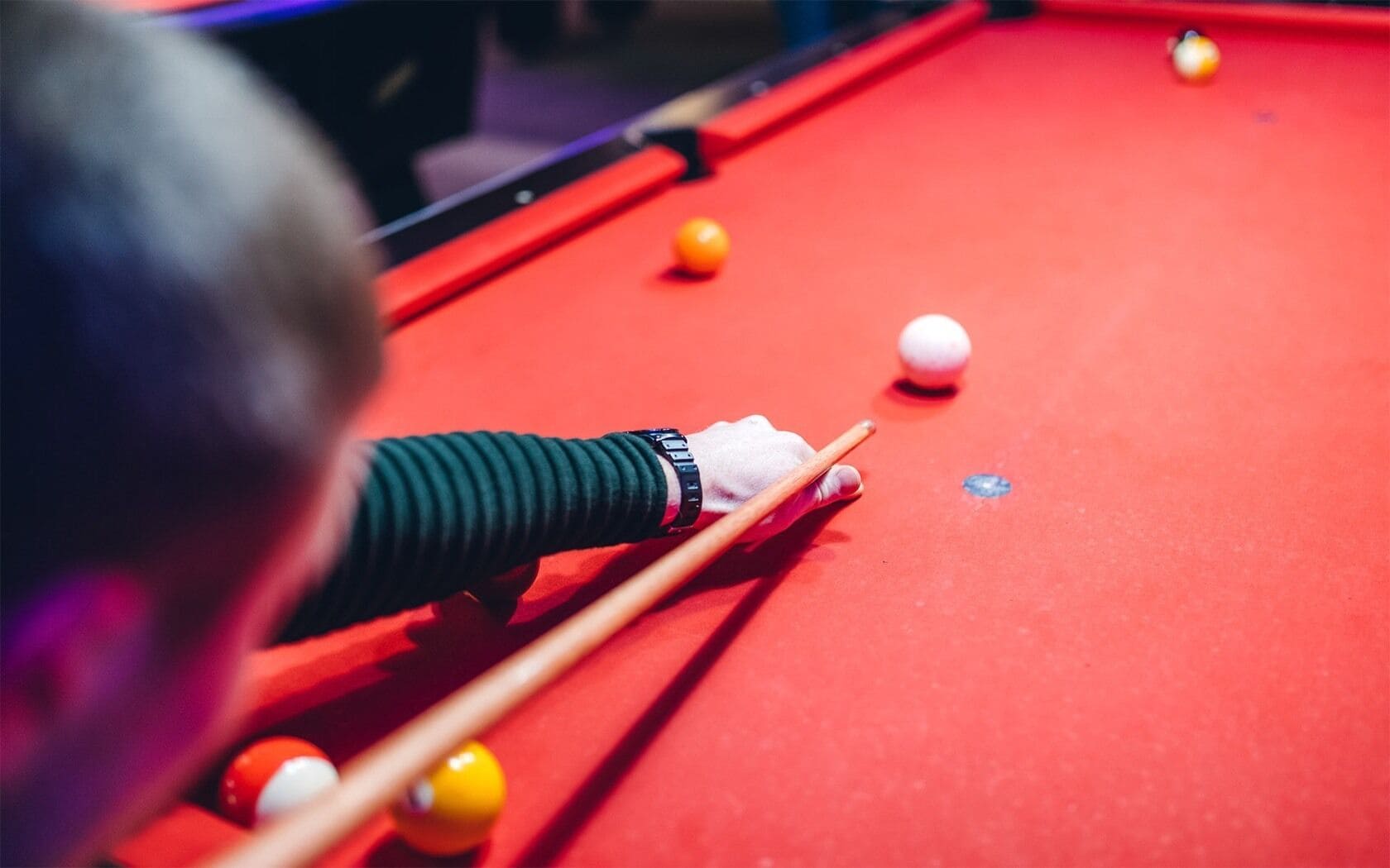 A close-up of a pool table with a red felt surface, a white cue ball, and several yellow and orange balls.