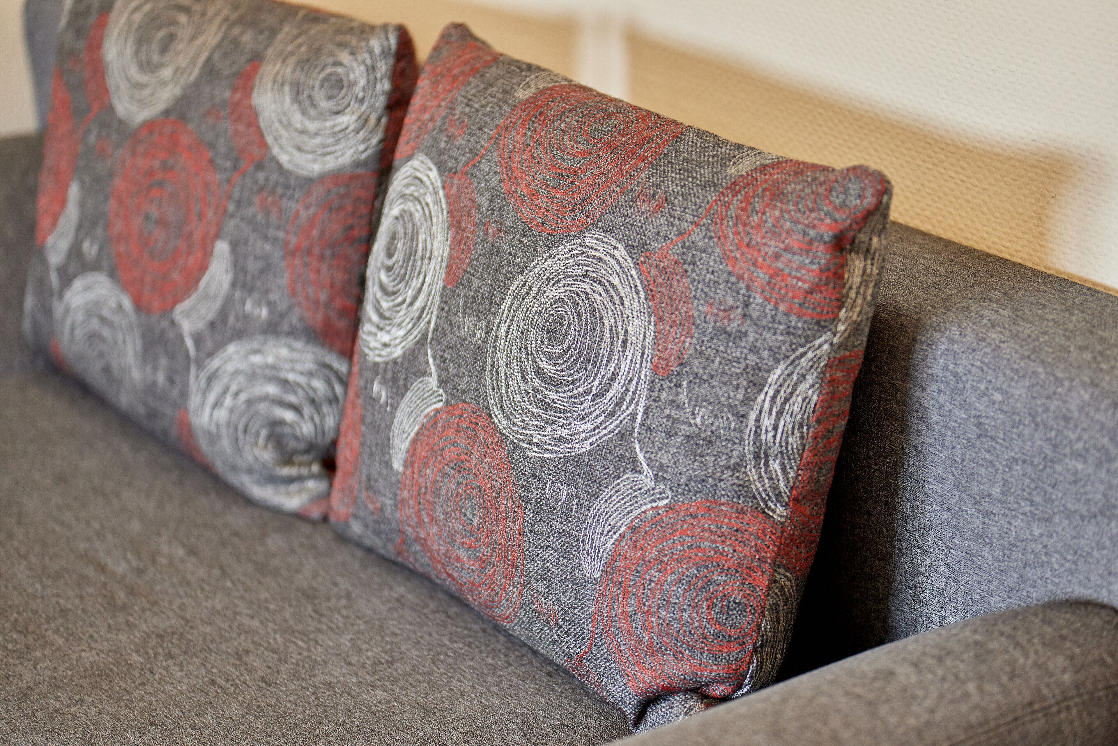 Un sofá gris con dos cojines decorativos con un estampado rojo y gris en espiral.