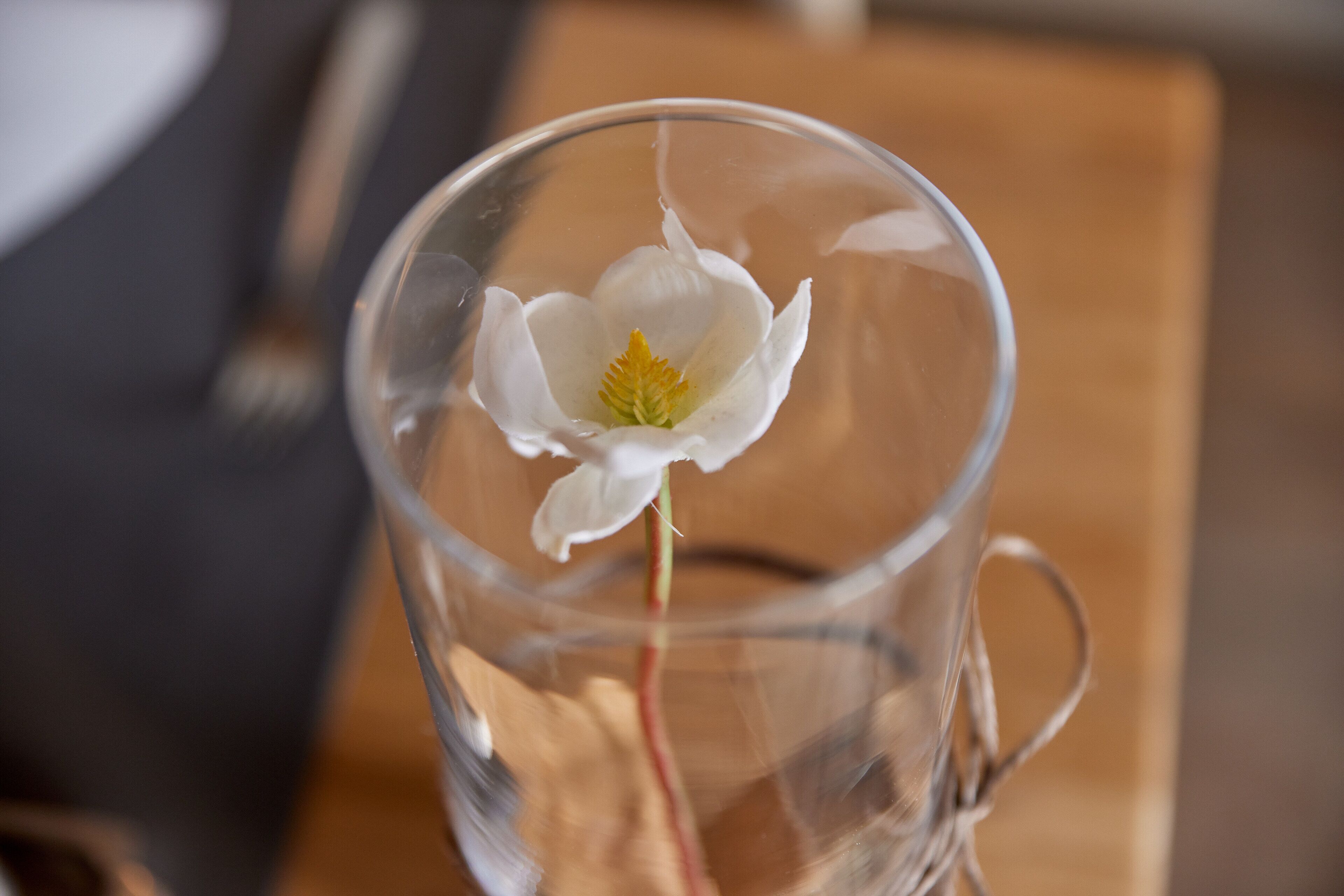 A clear glass cup with a white flower and a green center, placed on a wooden surface.