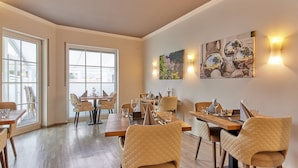 Un espace repas avec des tables et des chaises en bois, de grandes fenêtres et des luminaires fixés au mur.