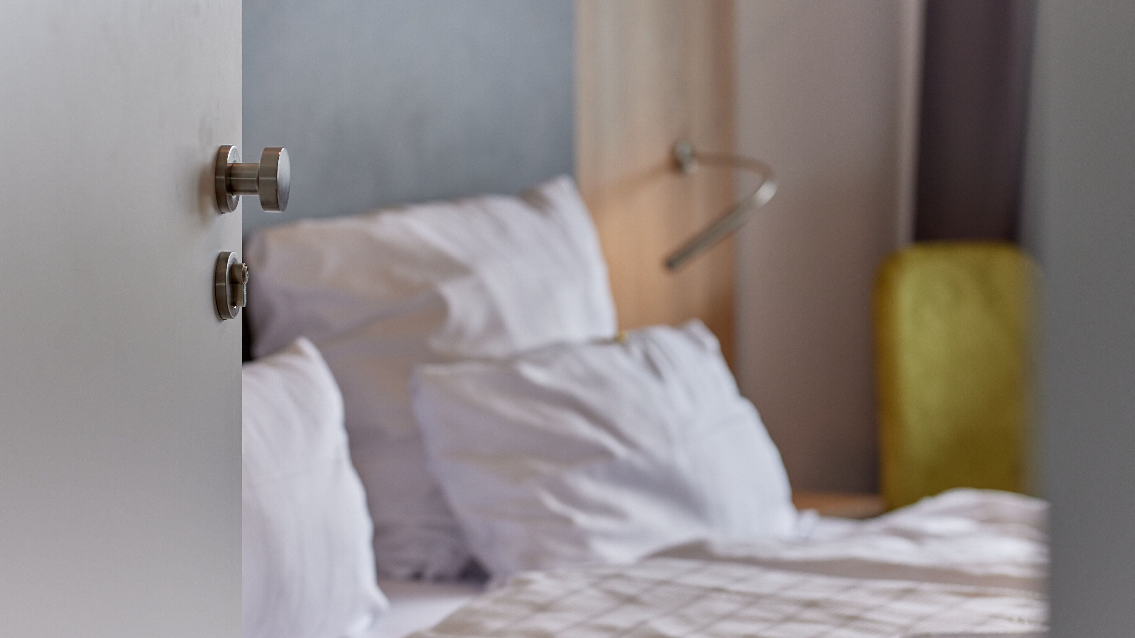 A hotel room with a bed, a bedside table, and a door.