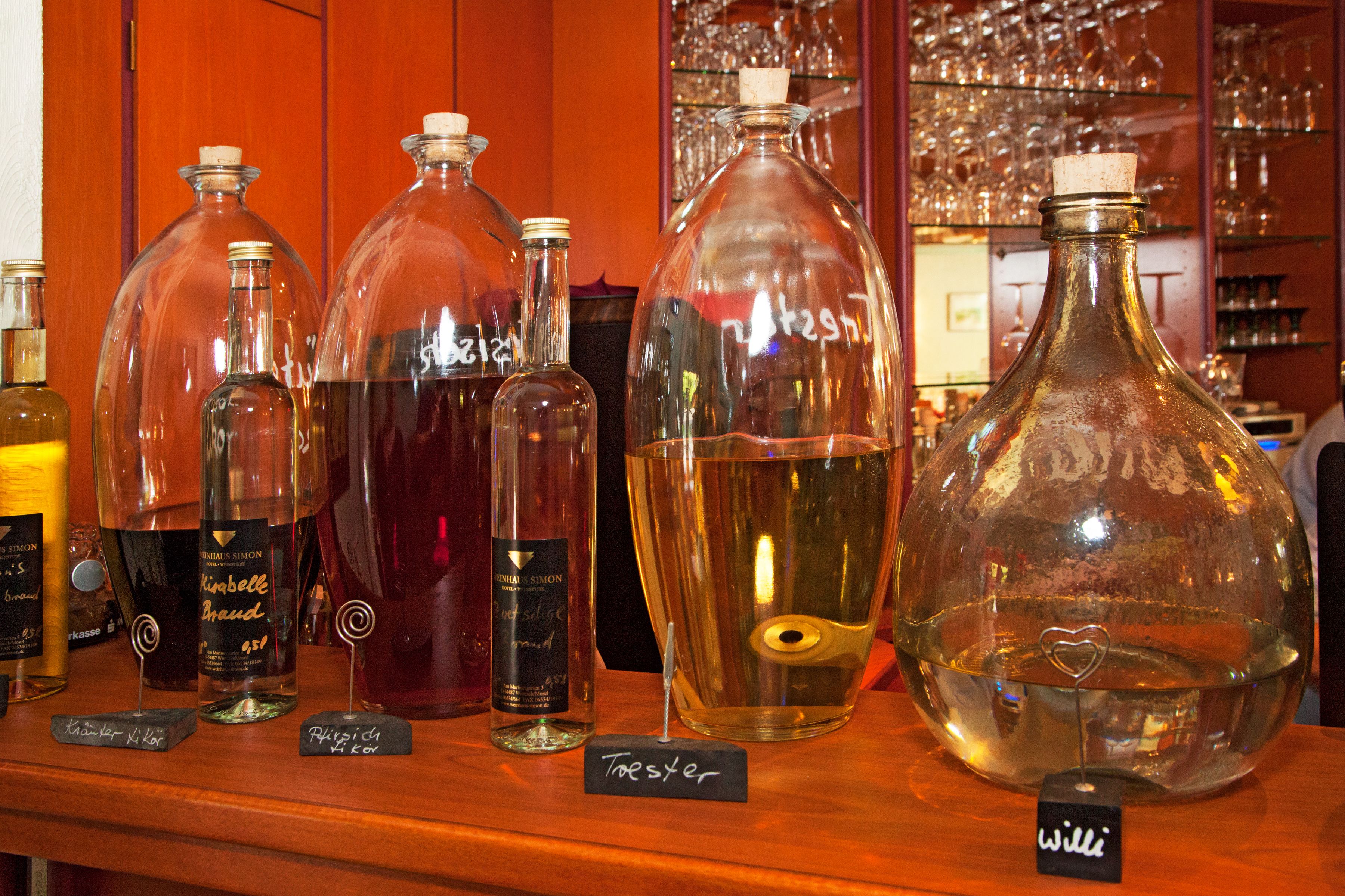 A variety of glass bottles with labels, some with corks, on a wooden shelf.