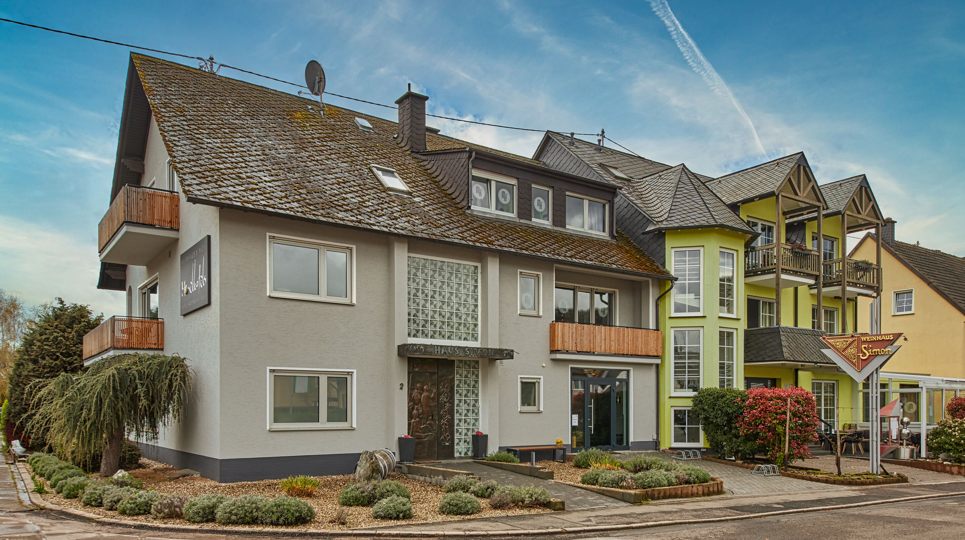 A row of modern houses with balconies, a visible entrance, and a well-maintained garden area.