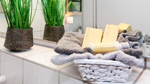 Une salle de bain avec des carreaux blancs, un miroir, deux plantes en pot, une serviette et des articles de toilette.