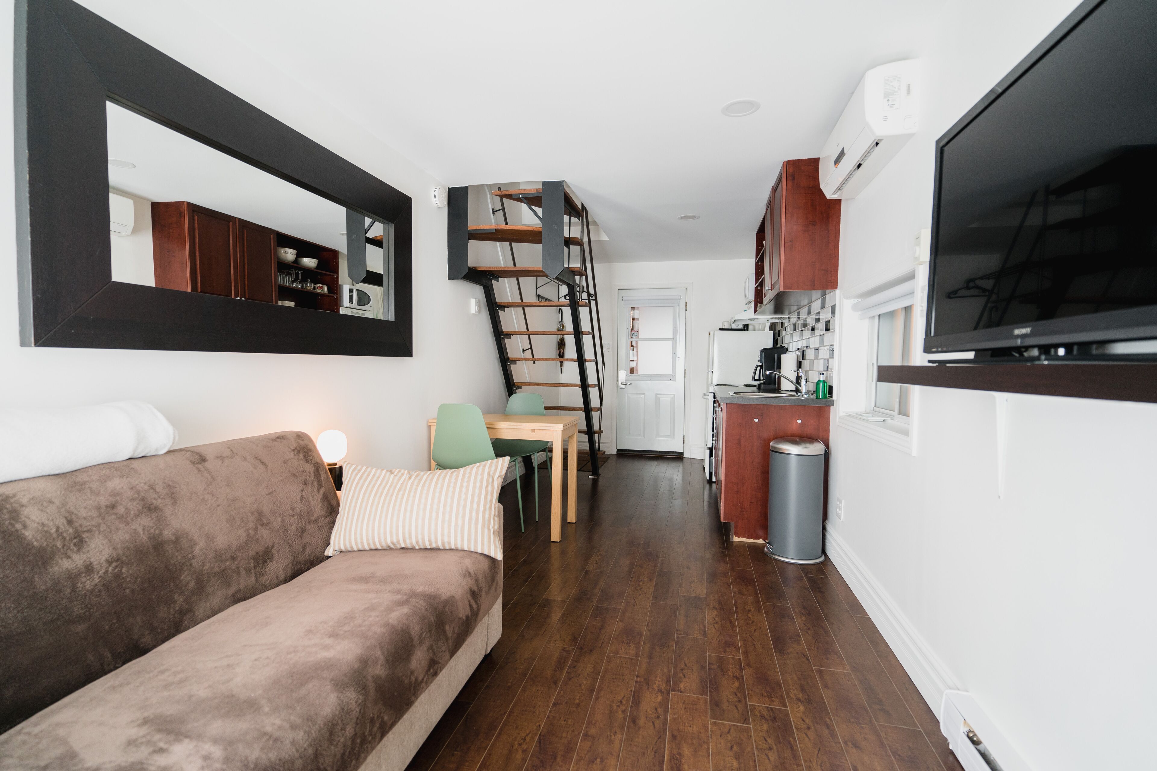Un espace de vie compact comprenant un canapé, un coin repas, une cuisine et un escalier.
