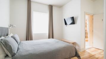 Ein Schlafzimmer mit Bett, Wandfernseher, Nachttisch und einem Fenster mit Vorhängen.
