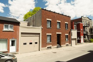 A row of brick townhouses with garage doors, a clear sky, and a tree.