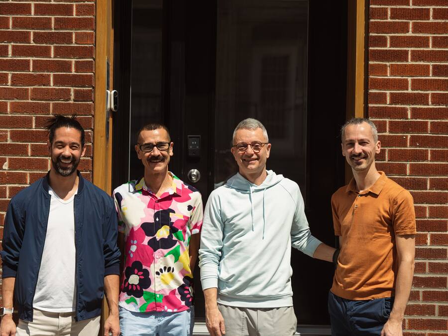 Four men standing in front of a brick building with a glass door.