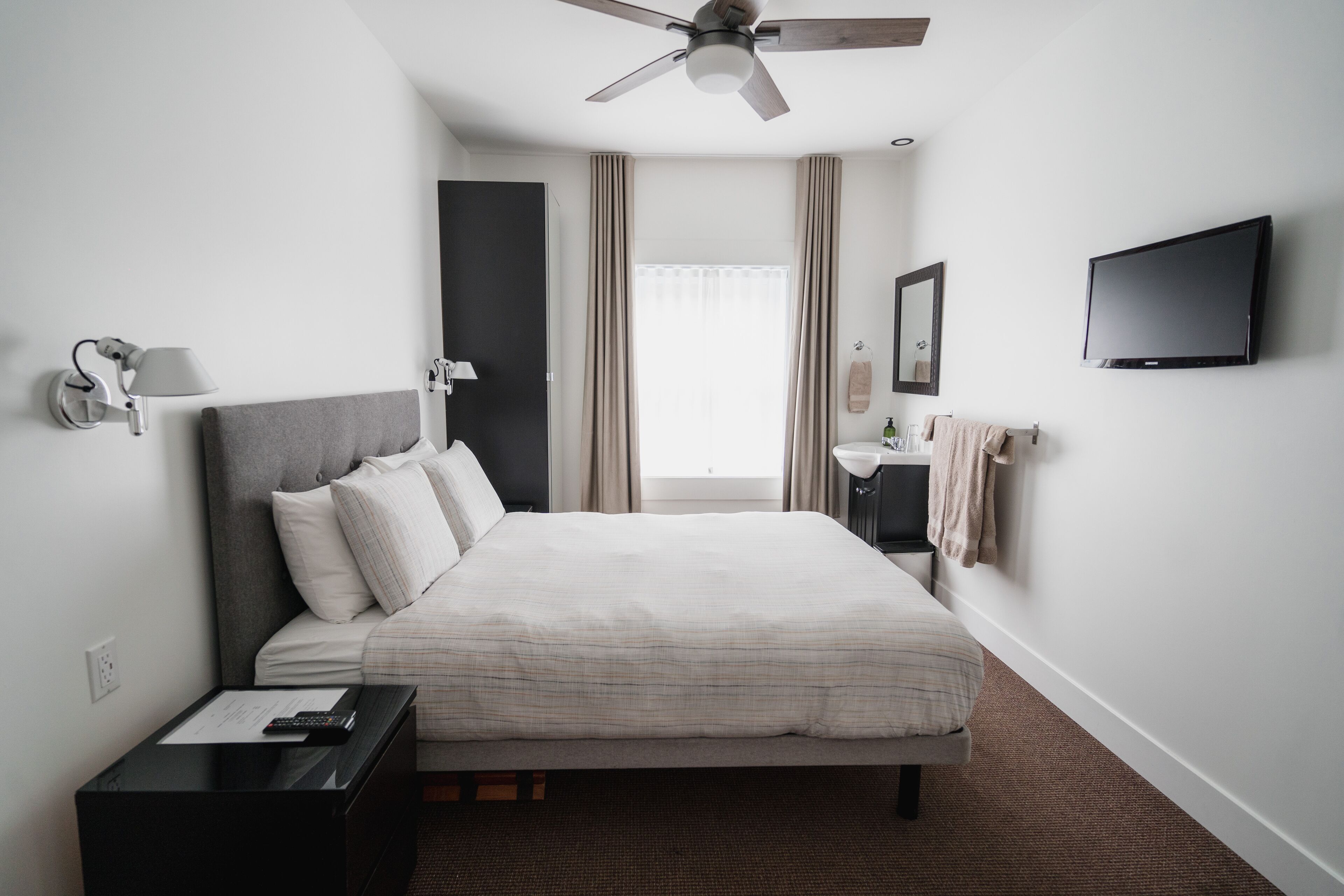 A hotel room with a bed, bedside table, lamp, TV, and a ceiling fan.