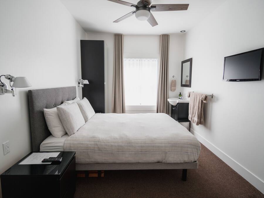 A hotel room with a bed, bedside table, lamp, TV, and a ceiling fan.