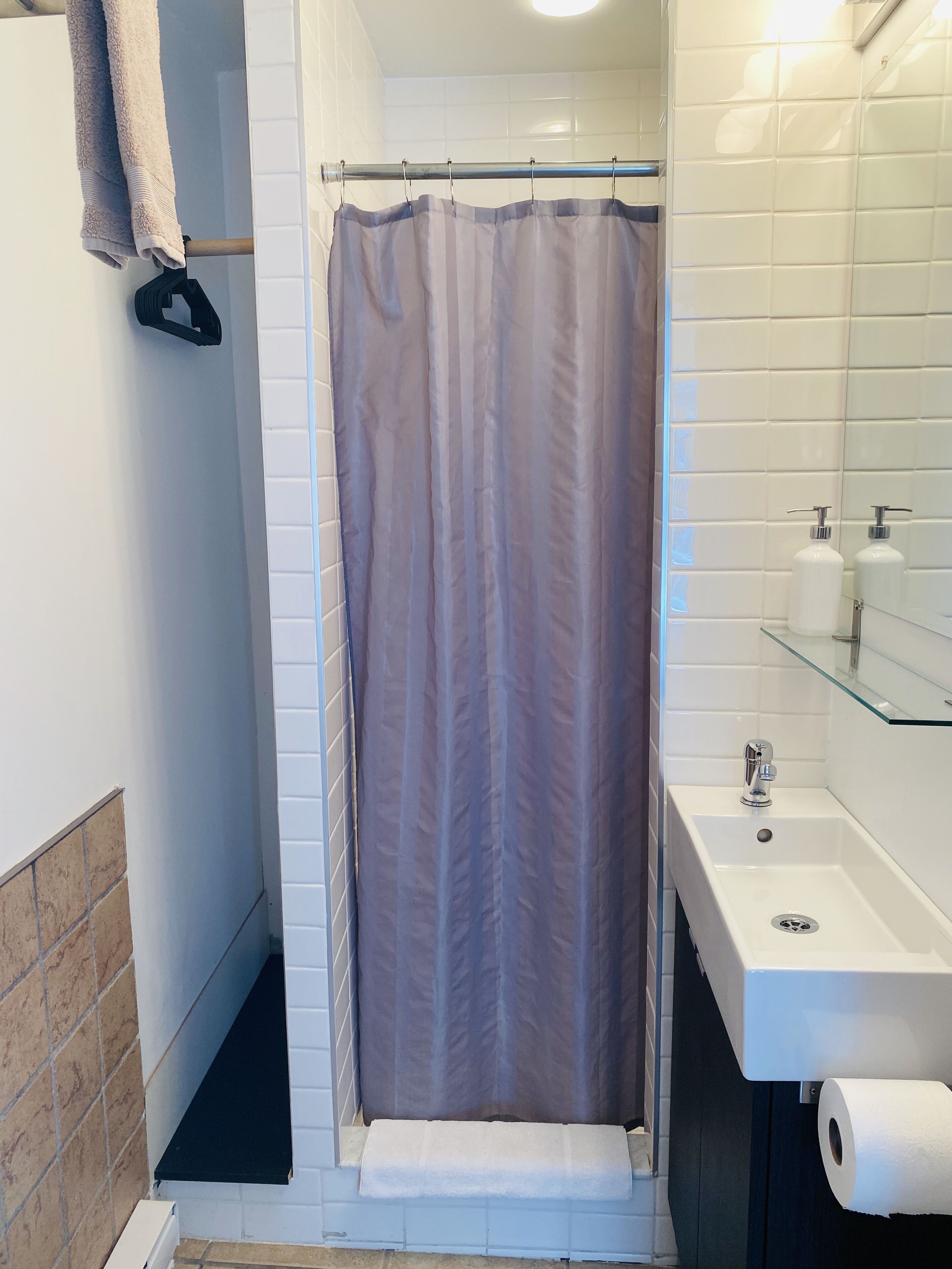 A bathroom with a shower curtain, a sink, and a toilet paper roll.