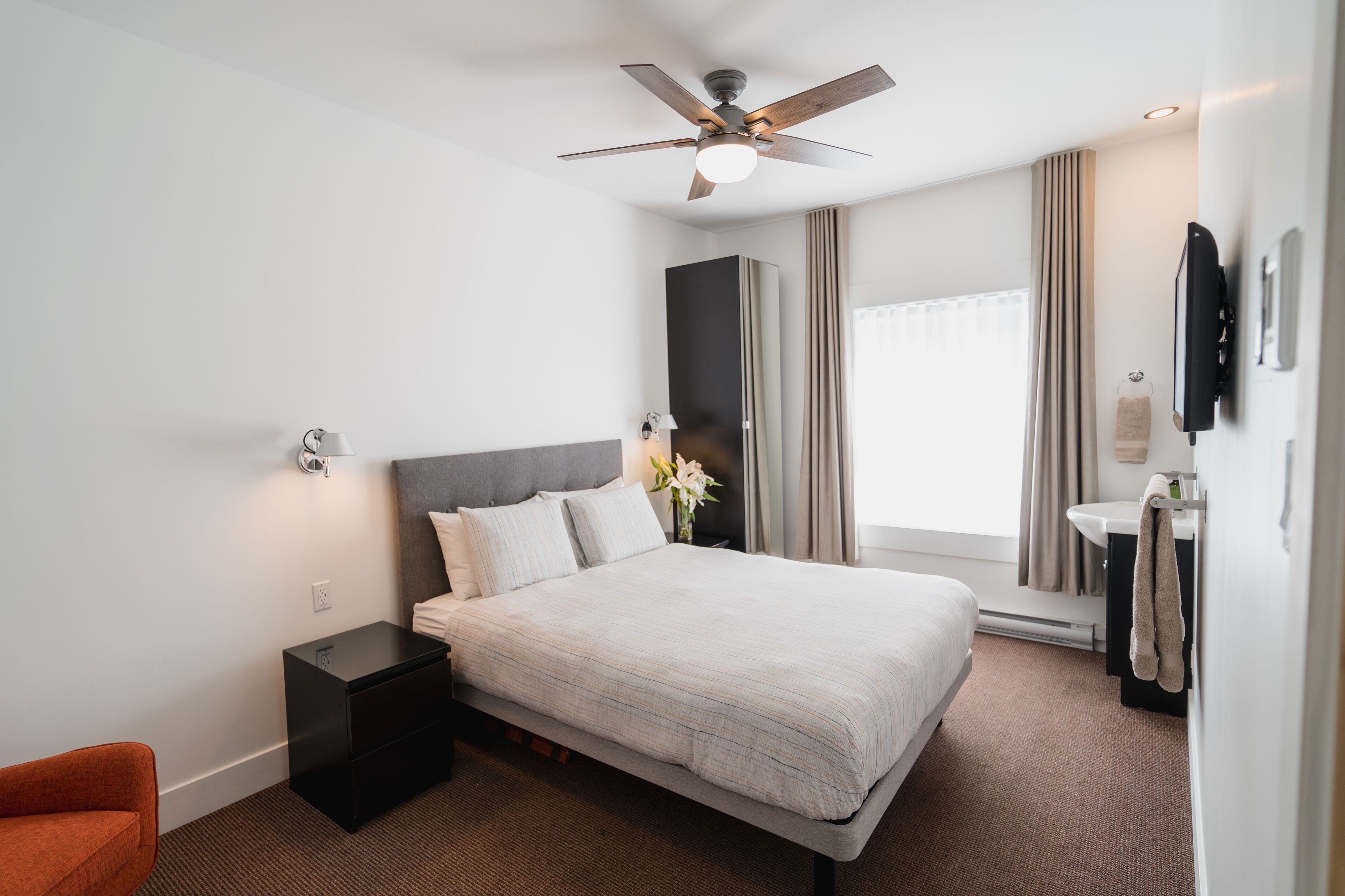 A hotel room with a bed, nightstand, wall-mounted TV, and a ceiling fan.