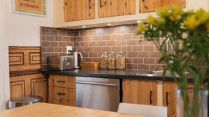 Una cocina con armarios de madera, encimera negra y lavavajillas de acero inoxidable. Hay frascos en la encimera y una planta en un florero.