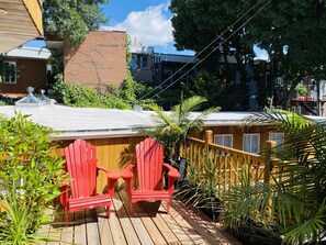 A wooden deck with red Adirondack chairs, surrounded by potted plants and a yellow fence.