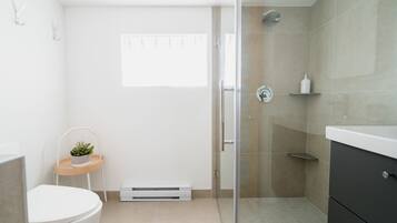 Ein modernes Badezimmer mit Toilette, Waschbecken, Dusche und einer kleinen Pflanze auf einem Beistelltisch.