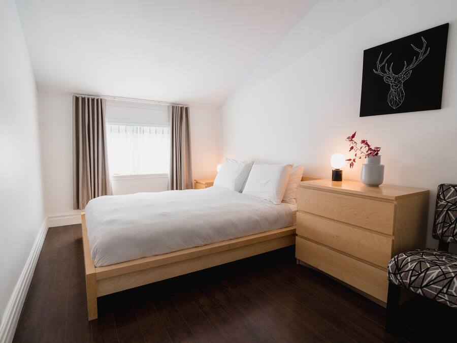 A modern bedroom with a wooden bed, a nightstand, a dresser, and a wall-mounted deer head artwork.