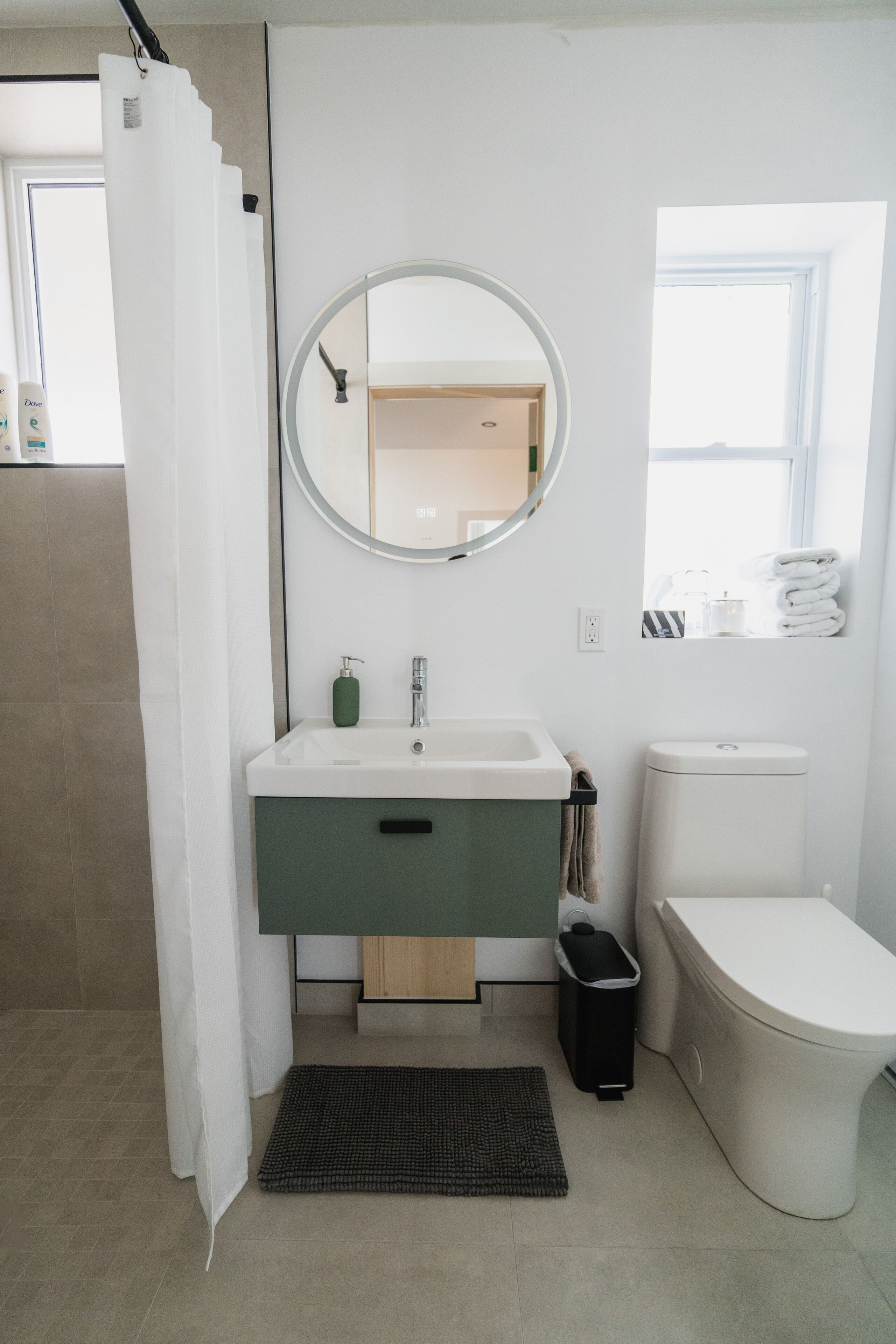A modern bathroom with a white sink, green cabinet, and a round mirror.