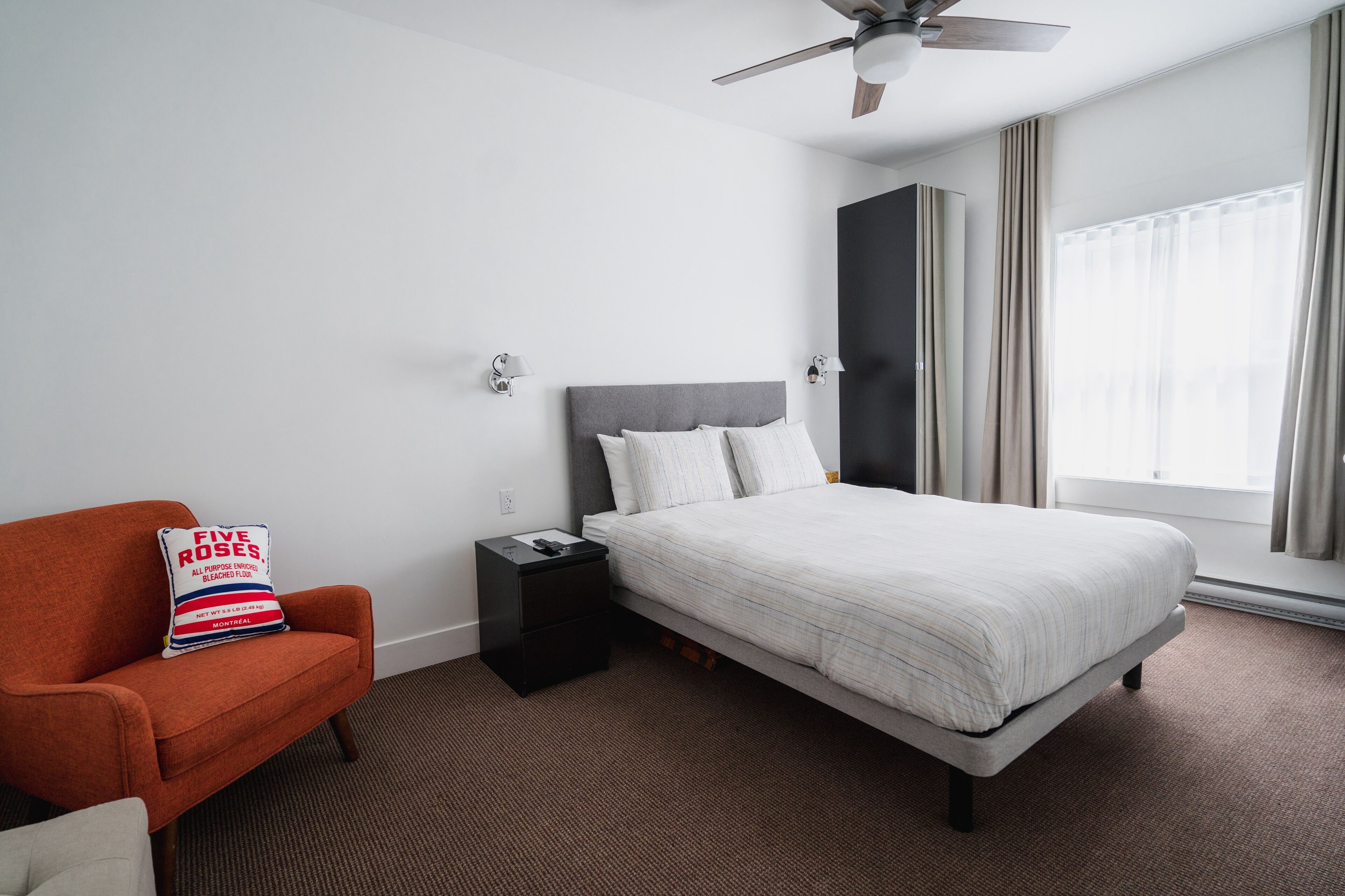 Habitación de hotel con cama, mesita de noche, una silla y ventilador de techo.